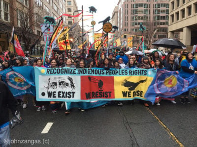 protestors carry a banner reading "recognize indigenous people's rights. we exist. we resist. we rise."