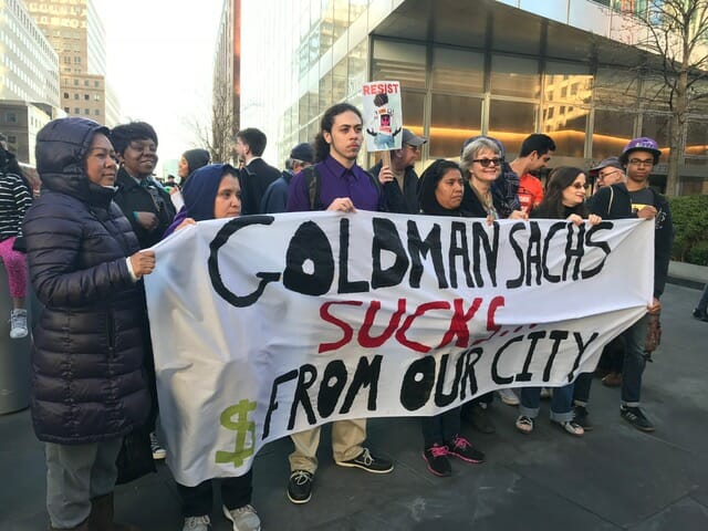 protestors hold a banner reading Goldman Sachs Sucks $ from our city