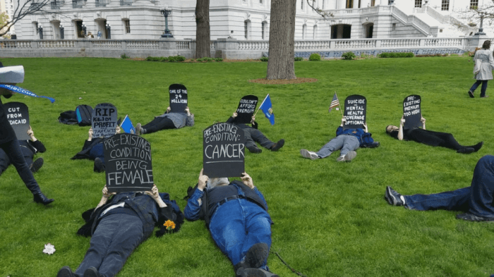 protestors lay in the grass with tombstone signs