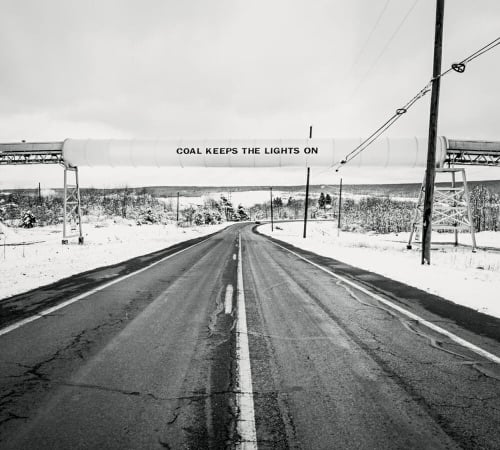 A banner reading “COAL KEEPS THE LIGHTS ON” is stretched over a snowy stretch of road in the Pennsylvania woods.