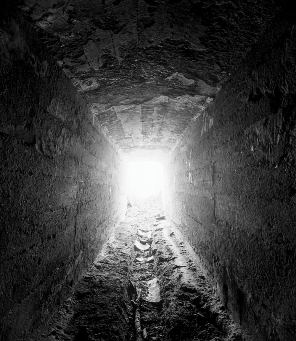 A photograph by Jeremy Blakeslee of a coal mine drainage tunnel in Centralia, PA with bright sunlight shining at the end.