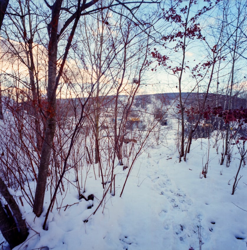 A photograph by Jeremy Blakeslee showing smoke rising behind bare trees in the snowy woods of Centralia, PA. A set of footprints winds through the snow.