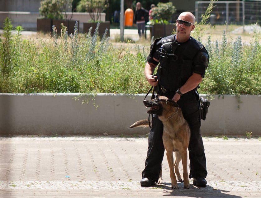 A German police officer stands guard at a neo-Nazi march. He holds back a German Shepherd by its collar.