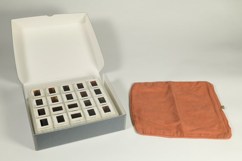 An orange cushion cover is placed next to a box of slides.