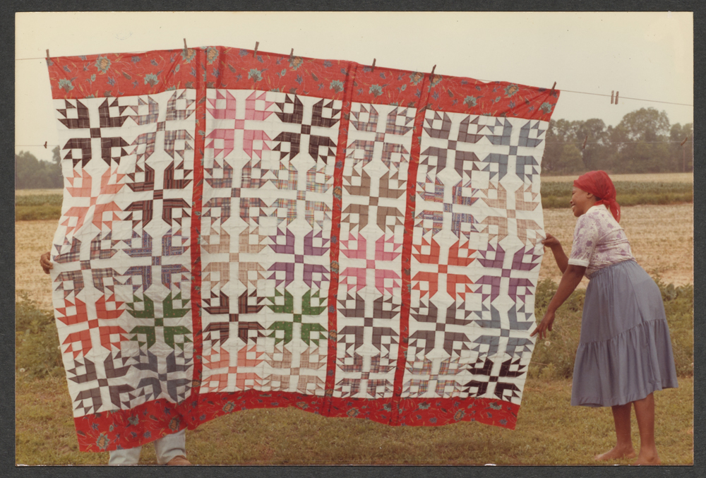 A woman hanging a quilt from a clothesline.