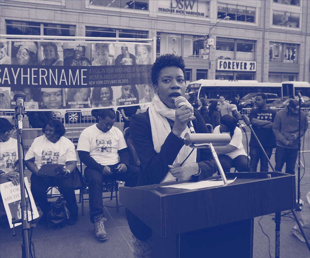 A young Black woman speaks on stage at a protest.