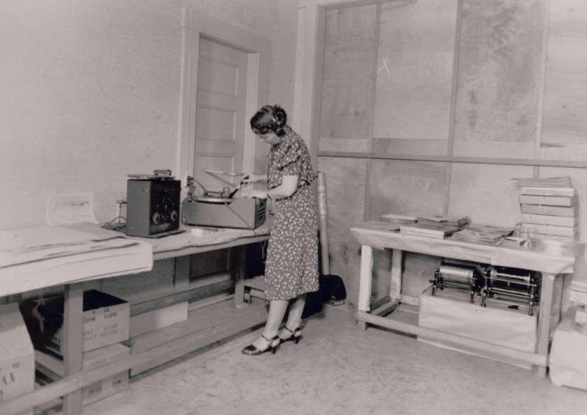 Black and white photo of a women copying vinyl recordings on an old turntable-like device.