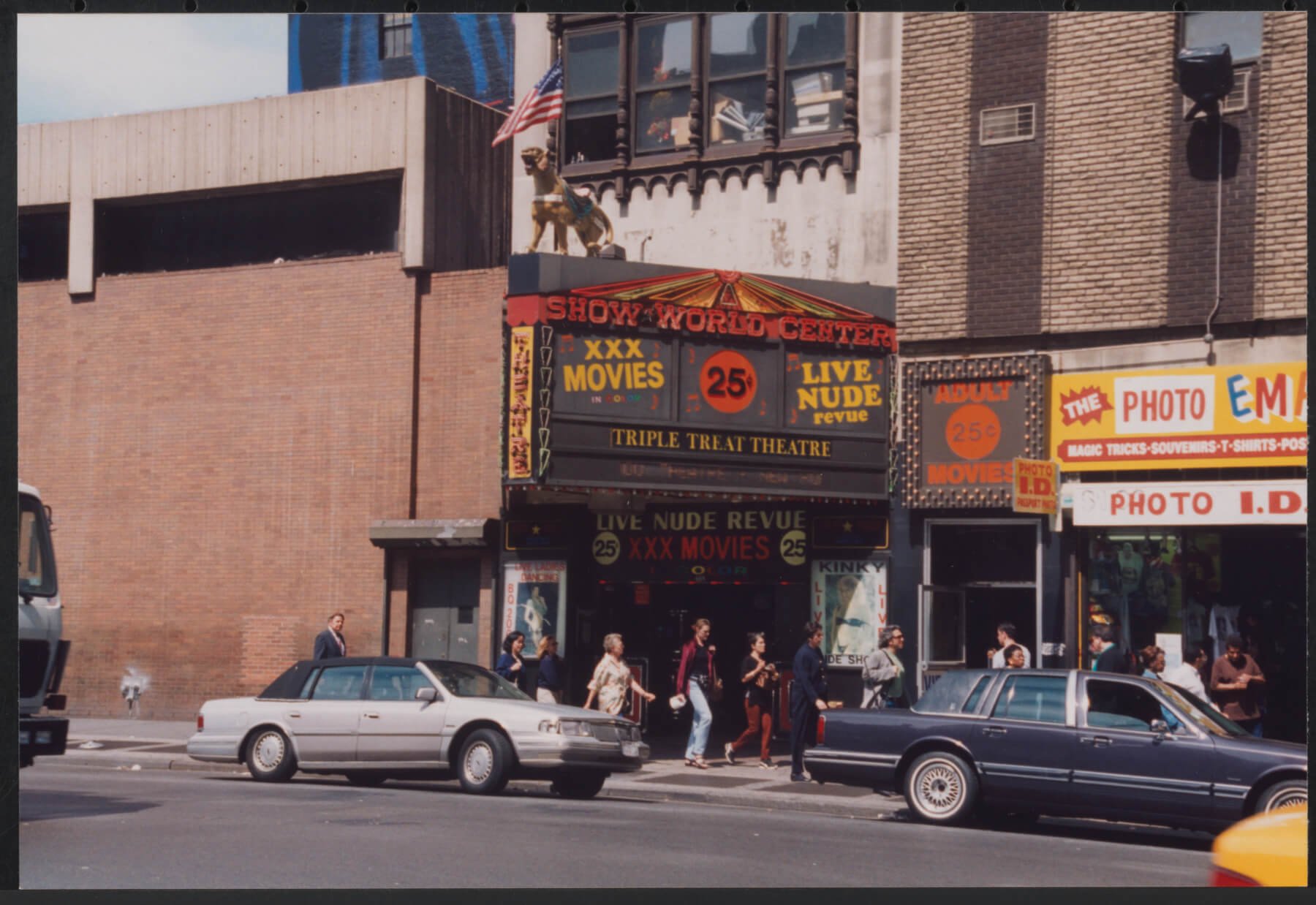 A photograph of a movie theater called “TRIPLE TREAT THEATRE” with signs that read “XXX MOVIES,” “25¢,” “LIVE NUDE revue.” 