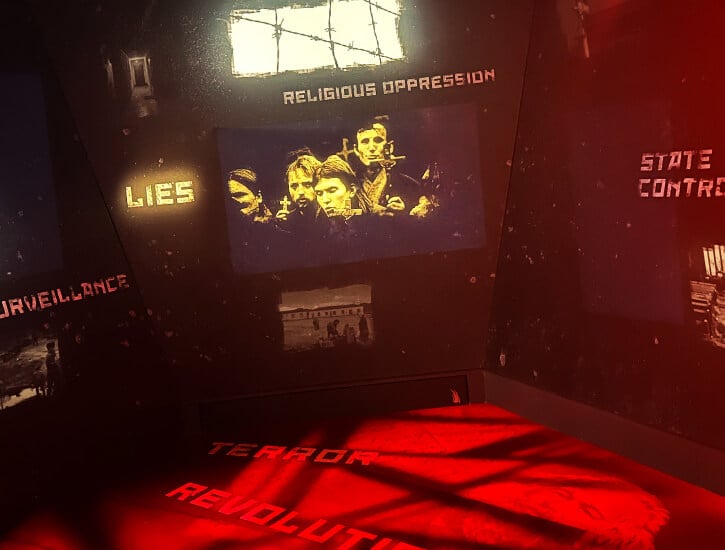 A dark room bathed in red light with text on the floor and walls: "LIES," "RELIGIOUS OPPRESSION," TERROR," "REVOLUTION."