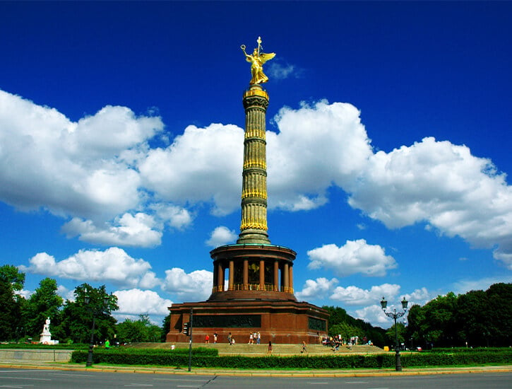 In the center of the photograph, a tall memorial column with a gold statue at the top. In the background, clouds drift by.