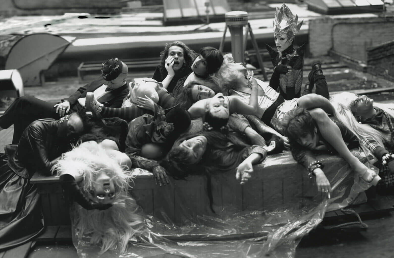 A group of individuals in elaborate costumes pile onto one another on a New York rooftop.