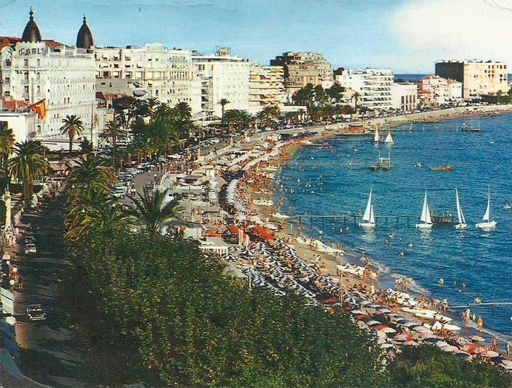 A row of white hotels along a beach crowded with people.