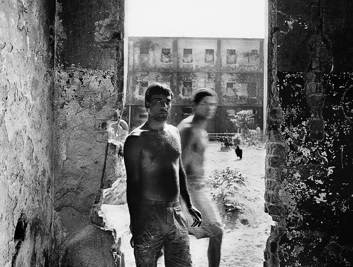 Two men stand in a doorway; the one of the right is blurred.