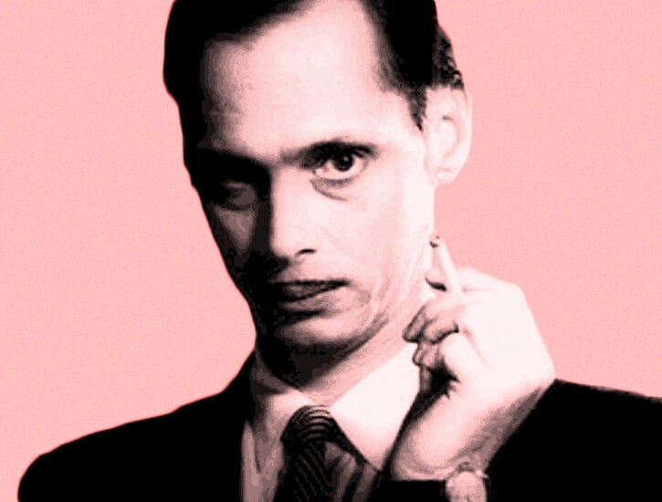 John Waters holds a cigarette.