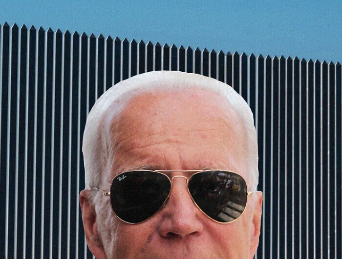 A portrait of President Biden in sunglasses. Behind him, the U.S.-Mexico border wall.