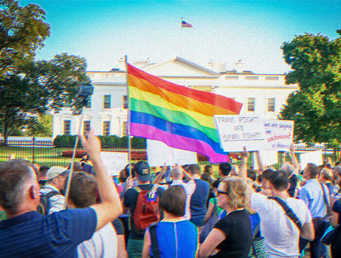 A group of protesters stand before the White House, one of them waving a large Pride flag.