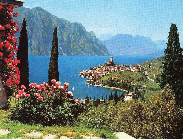 An Italian lake is shown in the distance, framed by plants.