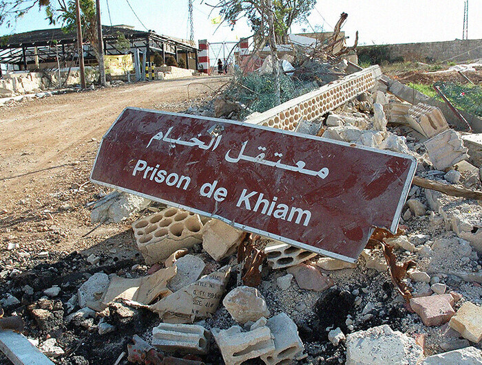 A dusty sign that reads "Prison de Khiam" lays in a pile of rubble.