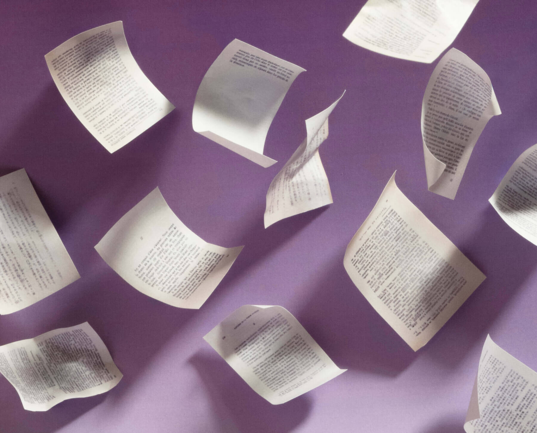 An image of papers mid-flight, with shadows suggesting that they have nearly landed onto a purple surface.
