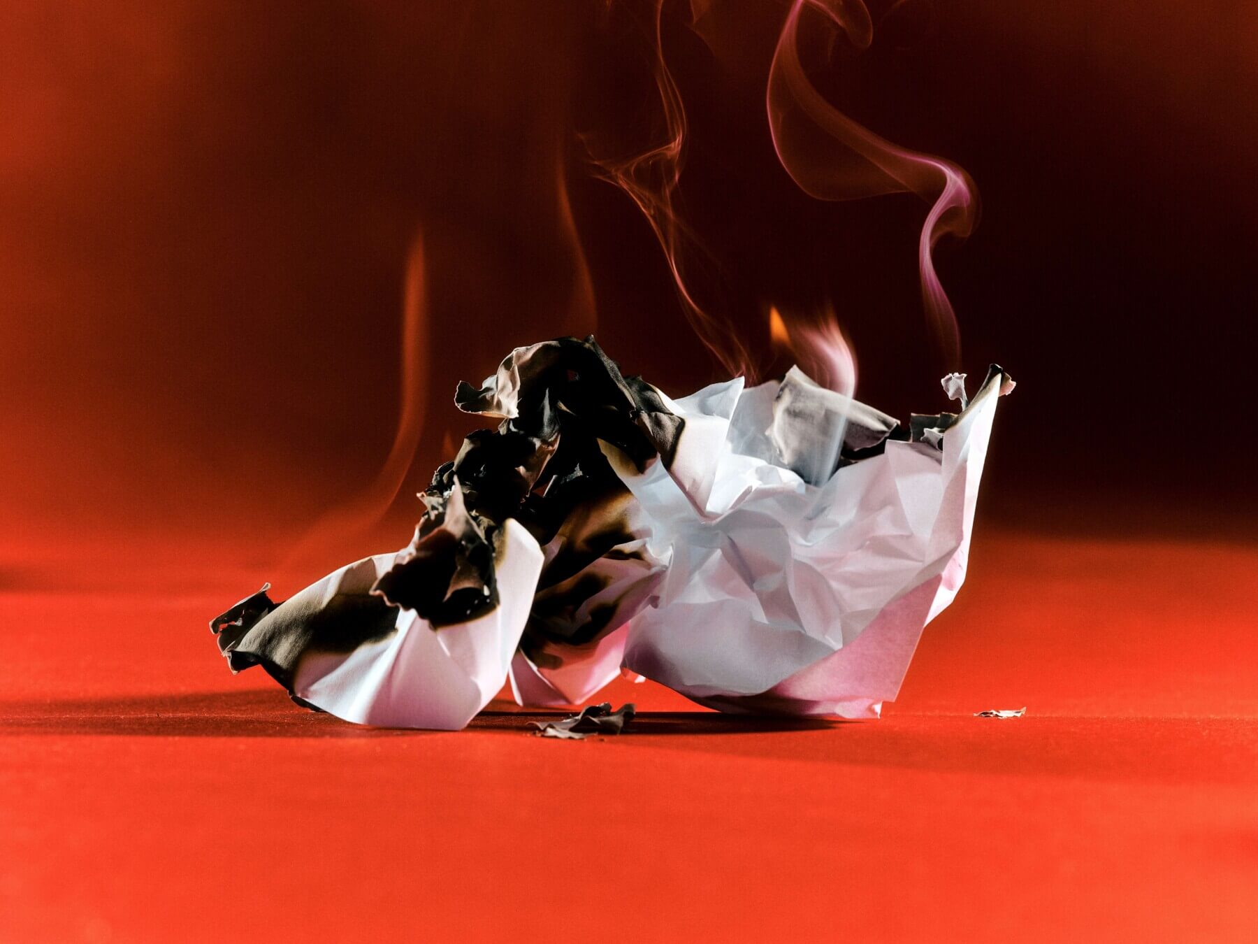 A crumpled piece of paper burns on a red backdrop.
