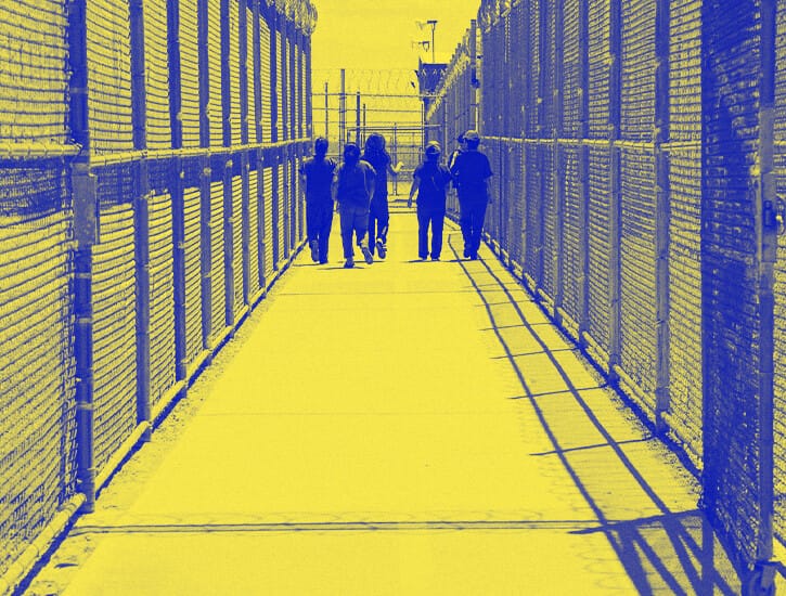 A group of detainees walk down a fenced in walkway at the Eloy detention center.