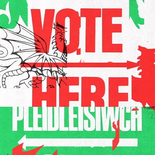 A poster reads “VOTE HERE” on the top and “PLEIDLEISIWCH YMA” on the bottom. Fragmented outlines and silhouettes of a dragon are laid on top of the image. The tone is bold and bright.