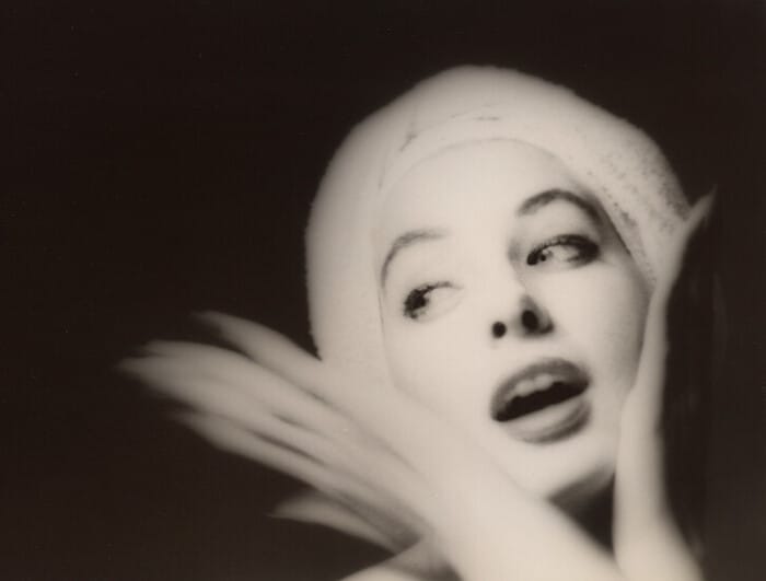 A young woman is photographed in black and white with her hands on her chin, looking to her right