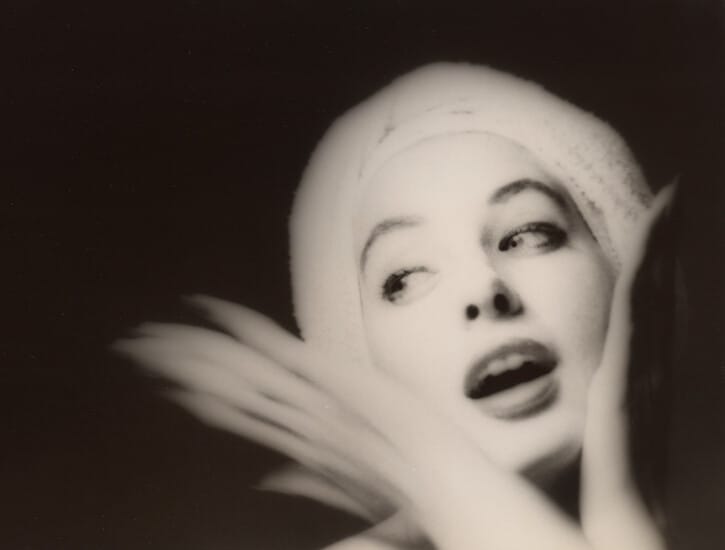 A young woman is photographed in black and white with her hands on her chin, looking to her right