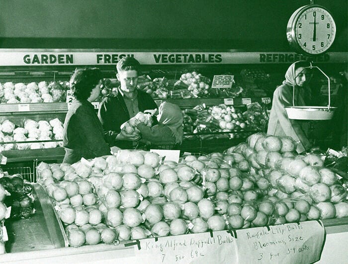 A man and a woman peruse produce in a grocery store.