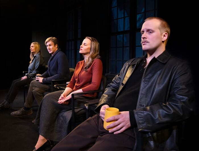 Four people sit in chairs on a stage: a man, an older woman, an older man, and a younger woman.