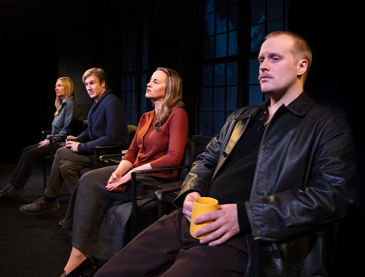 Four people sit in chairs on a stage: a man, an older woman, an older man, and a younger woman.
