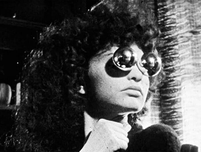 A woman with voluminous curly hair appears with two mirrored balls over her eyes.