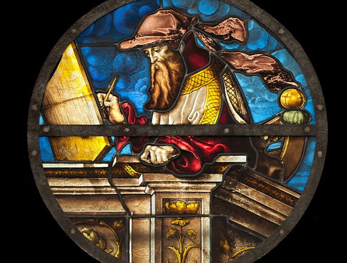 In a circular stained glass window, a portrait of the Prophet Isaiah. He is writing on a surface.