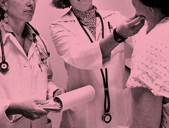 Two female doctors in white lab coats examine a patient.