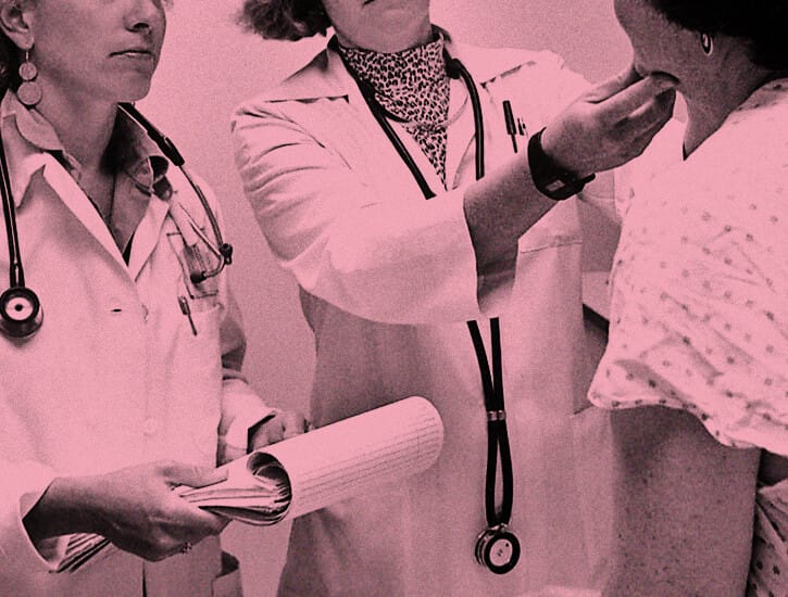 Two female doctors in white lab coats examine a patient.