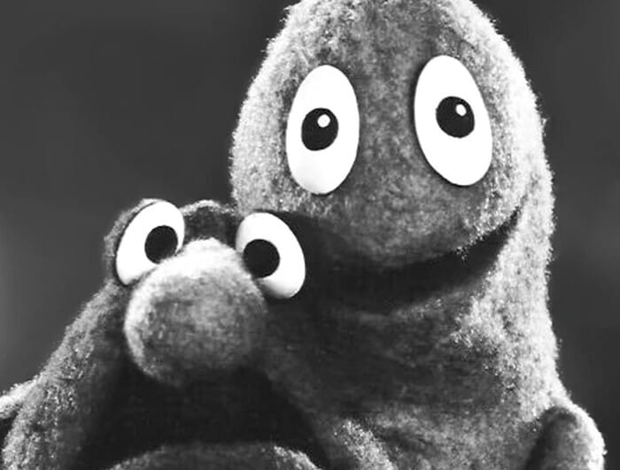 Two puppets with wide eyes sit side by side.
