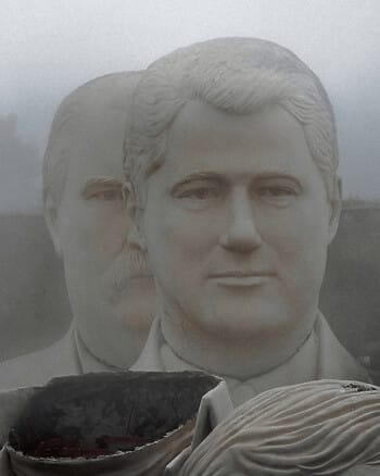 Two large statues of male heads sitting outside, surrounded by mist.