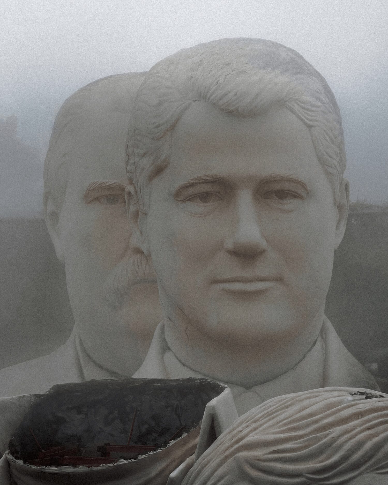 Two large statues of male heads sitting outside, surrounded by mist.